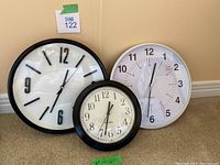 Three battery operated clocks: two quartz and one Westclox, displayed on floor against wall.