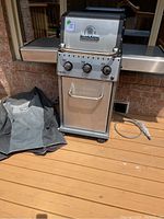 Grill unit with closed lid, folded cover beside and natural gas hose coiled on deck