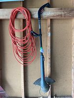 Photo showing the full Craftsman electric weedwacker and a long orange extension cord hung on a wooden wall.