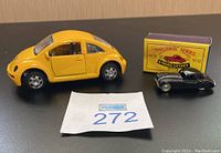 Yellow Volkswagen Classic Beetle die cast car with doors open sitting next to black Matchbox Series A Moko Lesney Jaguar and original yellow box, displayed on black surface.