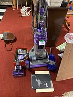 Full view of upright vacuum, accessories, manual, and feather duster arranged on carpet