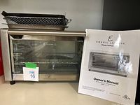 Front view of Emeril Lagasse Power AirFryer 360 with wire rack and baking pan on top, owner's manual beside it.