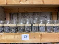 Shelf with seven clear glass Mason jars each labeled with a finishing nail size and filled with finishing nails.