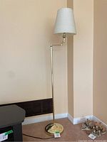 Full view of the brass floor lamp standing against a beige wall and carpeted floor, showing the lamp's height and structure.