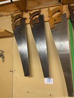 Three handsaws with wooden handles hanging on a wall, showing full blades and handles for size and condition.