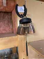 Wind chime hanging showing horseshoe top and three metal bells with black circular support.