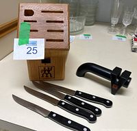Wooden knife block with 9 slots and J.A. Henckels logo, 4 steak knives with black handles, and knife sharpener all placed on a table.