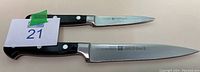 Two J.A. Henckels kitchen knives of different sizes on a flat surface, showing full length of blades and handles.