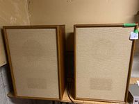 Front view of both speakers showing beige fabric fronts and wooden frames