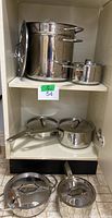 Wide view of stainless steel cookware set including large pasta pot, sauce pots, and lids inside a shelf.
