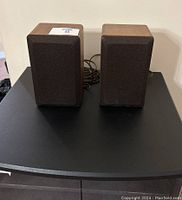 Pair of two Realistic Minimus-7W speakers side by side, showing wood veneer casing and cabling at the back