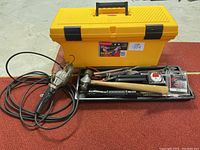 Photo showing the yellow Rubbermaid toolbox, 24 inch, with assorted tools including a hammer, tape measure, flashlight, and trouble light outside the box.