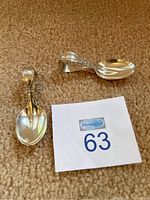 Two polished sterling silver baby spoons arranged on carpet next to a lot number card.