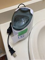White ultrasonic denture cleaner with transparent lid and attached power cord, placed on a bathroom counter.