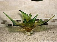 Front view of an abstract Murano art glass fruit bowl on counter, showing green and yellow glass with spiked points.