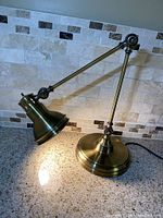 Brass adjustable table lamp placed on a countertop with tiled backsplash, lamp illuminated.