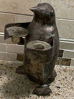 Front view of the silver plated penguin candle holder showing the shape, details, and two candle cups held by the penguin.