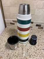 Thermos with cup lid, stopper, and colorful striped design on kitchen counter.
