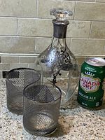 Glass decanter with silver overlay and two lowball glasses on a granite countertop with a Canada Dry Ginger Ale can for scale.