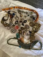 Group shot of vintage assorted jewelry including brooches, necklaces, rings, and earrings arranged on a white cloth.