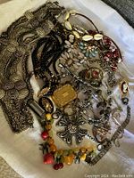 Full lot of vintage mixed jewelry including necklaces, brooches, rings, and pendants arranged on a white cloth.