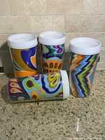 Four vintage collectible drinking cups with white rims and colorful psychedelic patterns on a countertop.