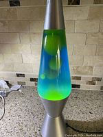 Full view of vintage lava lamp on a kitchen counter, showing the yellow lava floating inside blue liquid. Nickel metal base and top are visible. Lamp is lit and functioning.