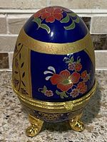Front view of the egg shaped trinket box showing cobalt blue background with colorful hand painted flowers and gold detailing.