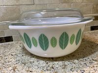 Side view of the vintage Modglass bowl with green leaf designs, showing the clear glass lid resting on top.