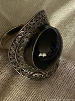 Close-up photo of ring showing the large black onyx cabochon and ornate silverwork with swirled and dotted patterns.