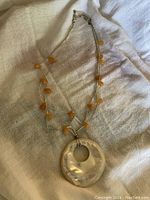 Full view of the necklace laid flat showing the mother of pearl pendant, triple strand beaded necklace with yellow stones.