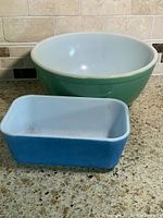 Blue rectangular loaf pan with white interior and green round mixing bowl with white interior, shown on countertop.