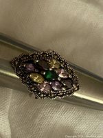 Top view of the ring showing the marquise cut multicolored stones and marcasite border on a metal ring sizer.