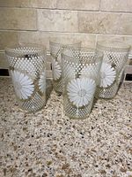 Four vintage glass tumblers with white daisy and white polka dot patterns shown standing on a speckled countertop against a tiled backsplash.