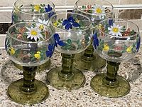 Six vintage Roemer Salzberg glass goblets arranged on a kitchen counter showing the floral hand-painted design and green pedestal bases clearly.