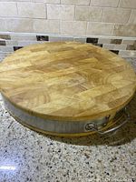 Side view of the round wooden cutting board showing the metal frame and handle attachment.