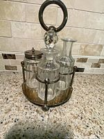 Front angle of the vintage silver plated caster set displaying the round base, central handle, and four bottles with lids and stoppers arranged inside.