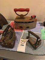 Top and angled view of four antique irons showcasing wooden handles and metal bodies with rust.