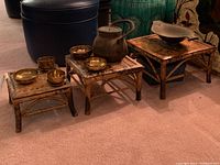 Wicker nesting stools with brass tea set including bowls and teapot arranged on top, showing wear on stools and brass items.