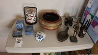Top view of the full collection showing several ceramic boxes, a large ornate bowl, wooden hand sculptures, a wooden figure, and a small hexagonal box