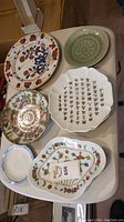 Six china plates shown on a table with various colorful and embossed designs, some chipped.