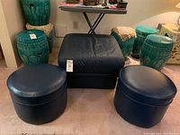 Full set of three blue leather ottomans arranged on carpet with surrounding decor, showing overall condition and details.
