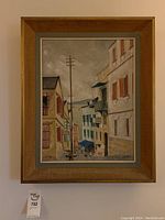 Frontal view of framed painting depicting narrow coastal village street