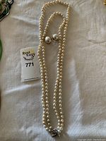 Full view of pearl necklace laid out with matching earrings and auction tag