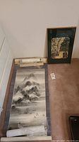 Photo showing a large traditional Asian scroll painting laid flat with fabric border and adjacent framed art piece on floor.