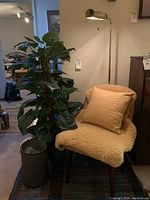 Full view of setup with chair covered in sheepskin throw and pillow, faux plant in basket and floor lamp in background