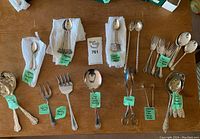 Overview of assorted sterling and silver plate teaspoons and sugar cube tongs on wood surface