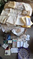 A large assortment of assorted table linens including embroidered napkins, folded linens, and small items laid out on a table and on the floor.