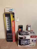 Photo showing Yamaha PSS-180 keyboard box with Yamaha PA-1 power adapter on top, Philips cassette tape, small red and silver portable radio, and boxed TEAC SL-D80 stereo system.