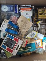 Top view of assorted small hardware items including aluminum nails, screws, plastic anchors, flat washers in original packaging and loose items.